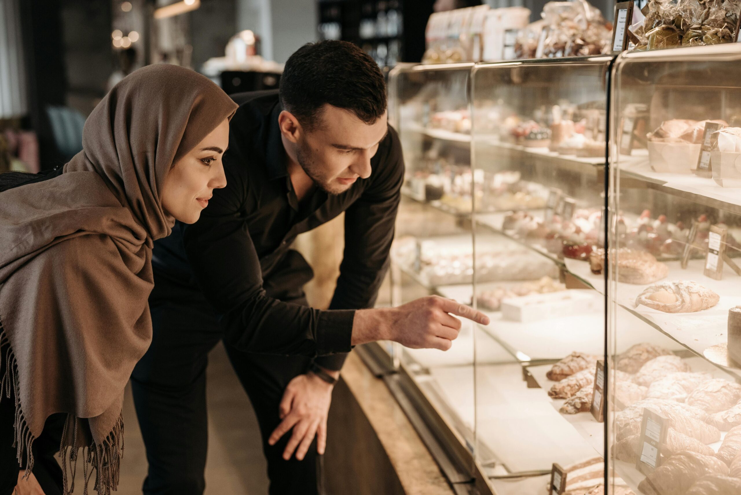 A couple selecting pastries at a bakery display case, highlighting their choice in a modern shop setting.